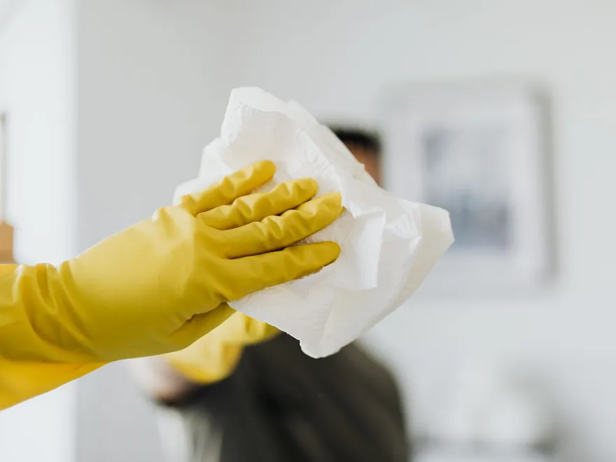 Cleaner in yellow rubber gloves wiping a mirror with a cloth