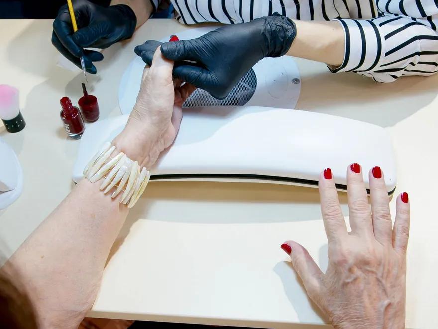 Nail technician applying red polish to a client's nails at a salon table